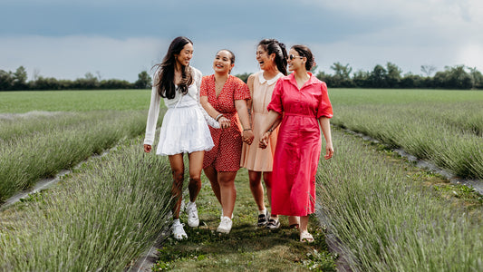 Four female friends smile and hold hands while walking through green rows of lavender