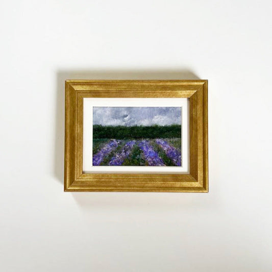 Small fine art print of rows of purple lavender with green tree line in distance. Golden frame with white matte.