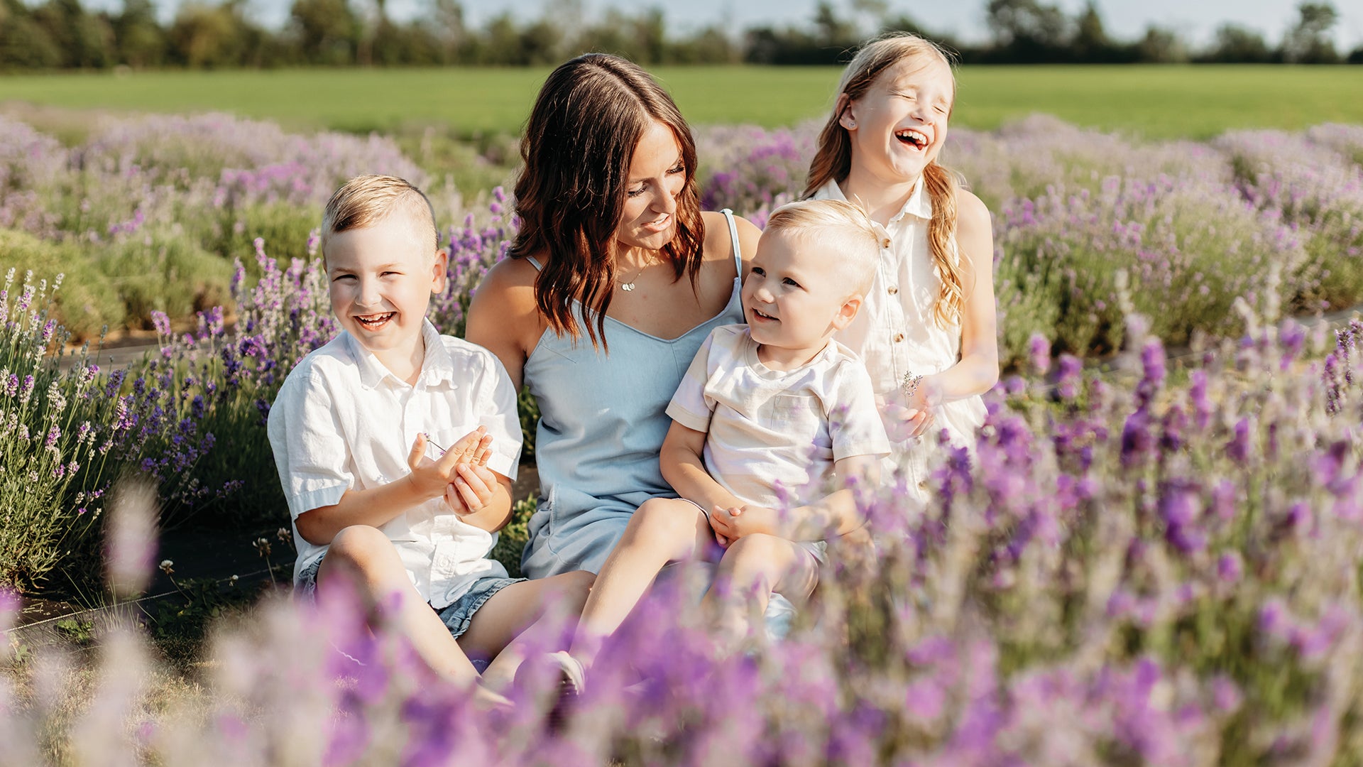 Three white children sit laughing and smiling with their Mom between rows of bright purple lavender