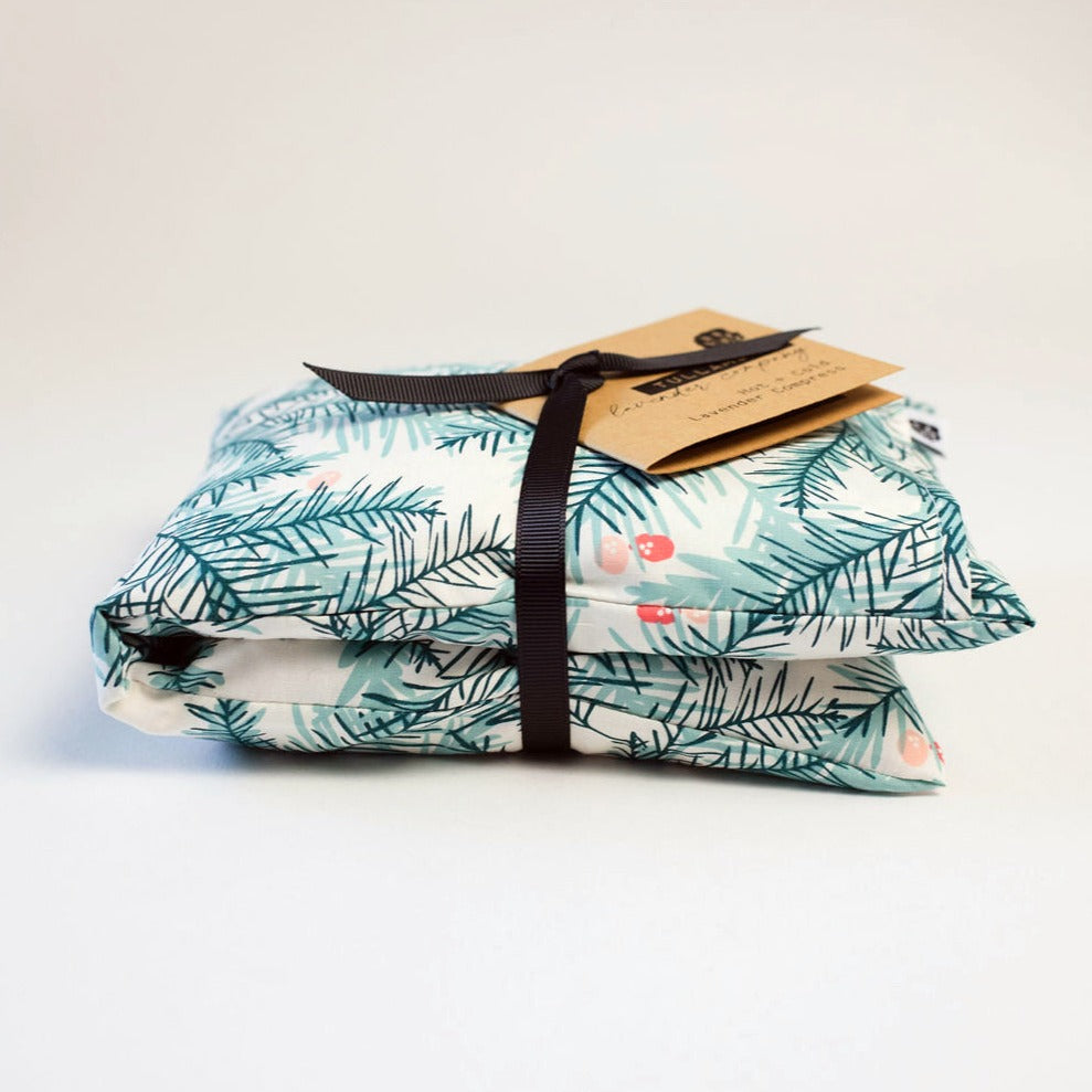 Compress folded with black ribbon and brown tag. Compress fabric is green pine leaves with red holly berries