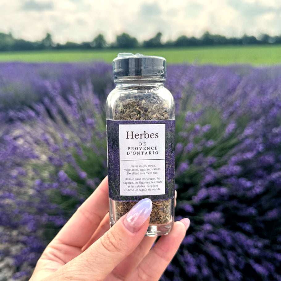 Hand holding a bottle of Herbes de Provence d'Ontario in front of a lavender field