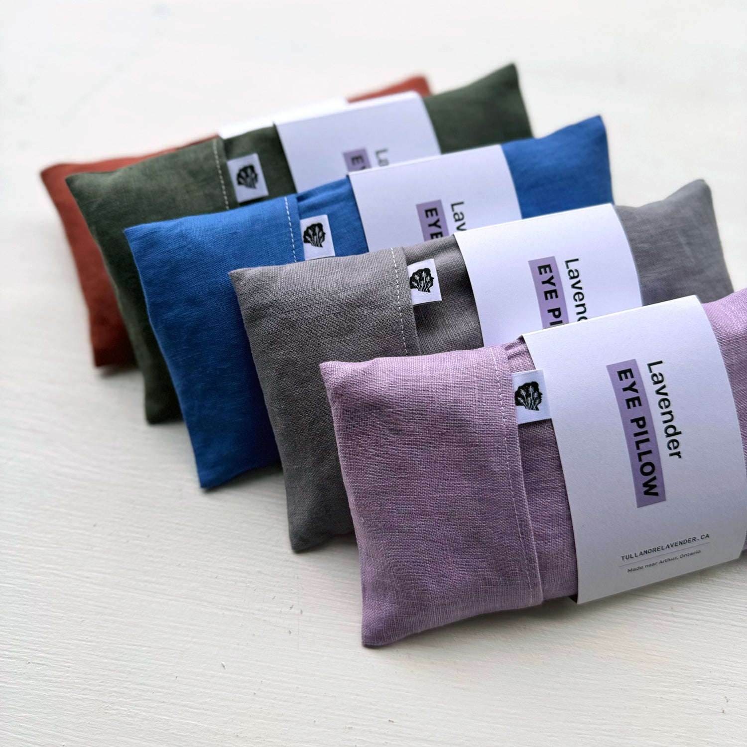 Five eye pillows lined up together on white table with labels that say "Lavender Eye Pillow"