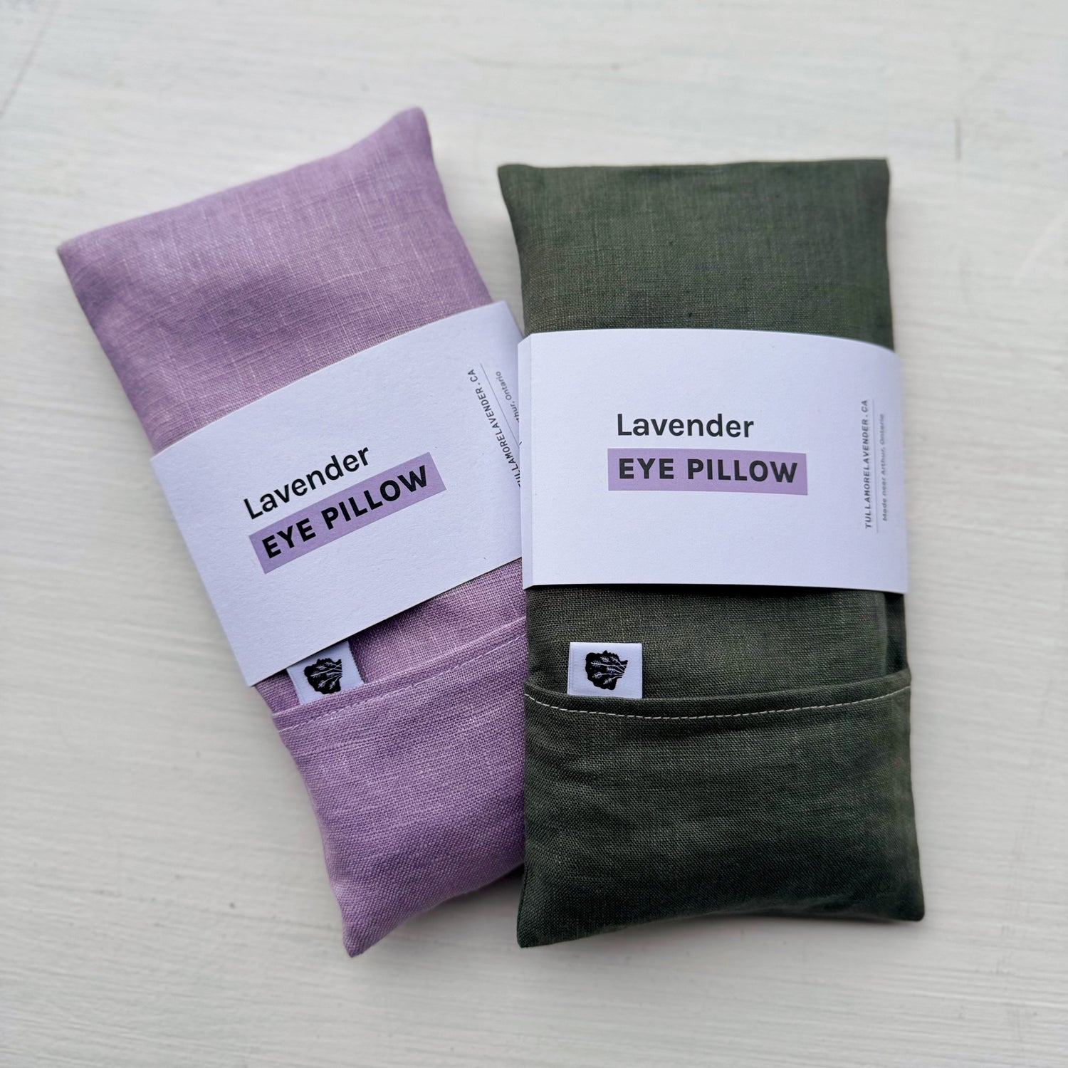 Purple and sage green eye pillows with white labels on them that say "Lavender Eye Pillow"