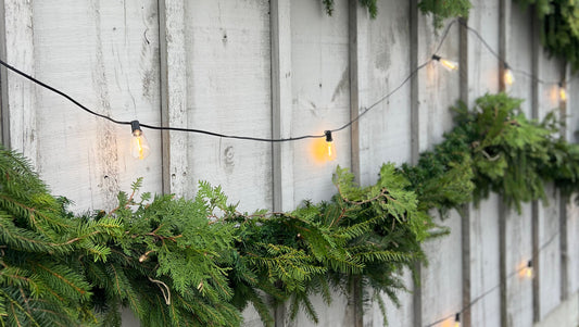 Green garland and vintage string lights hang on grey wooden wall