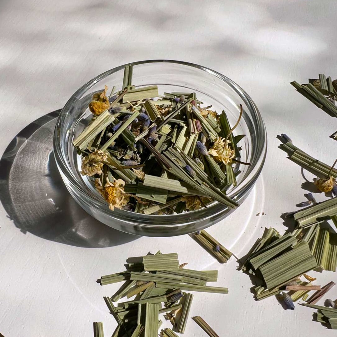 Loose leaf tea in small glass bowl and on white table. Green leaves, blue lavender buds and yellow dried flowers
