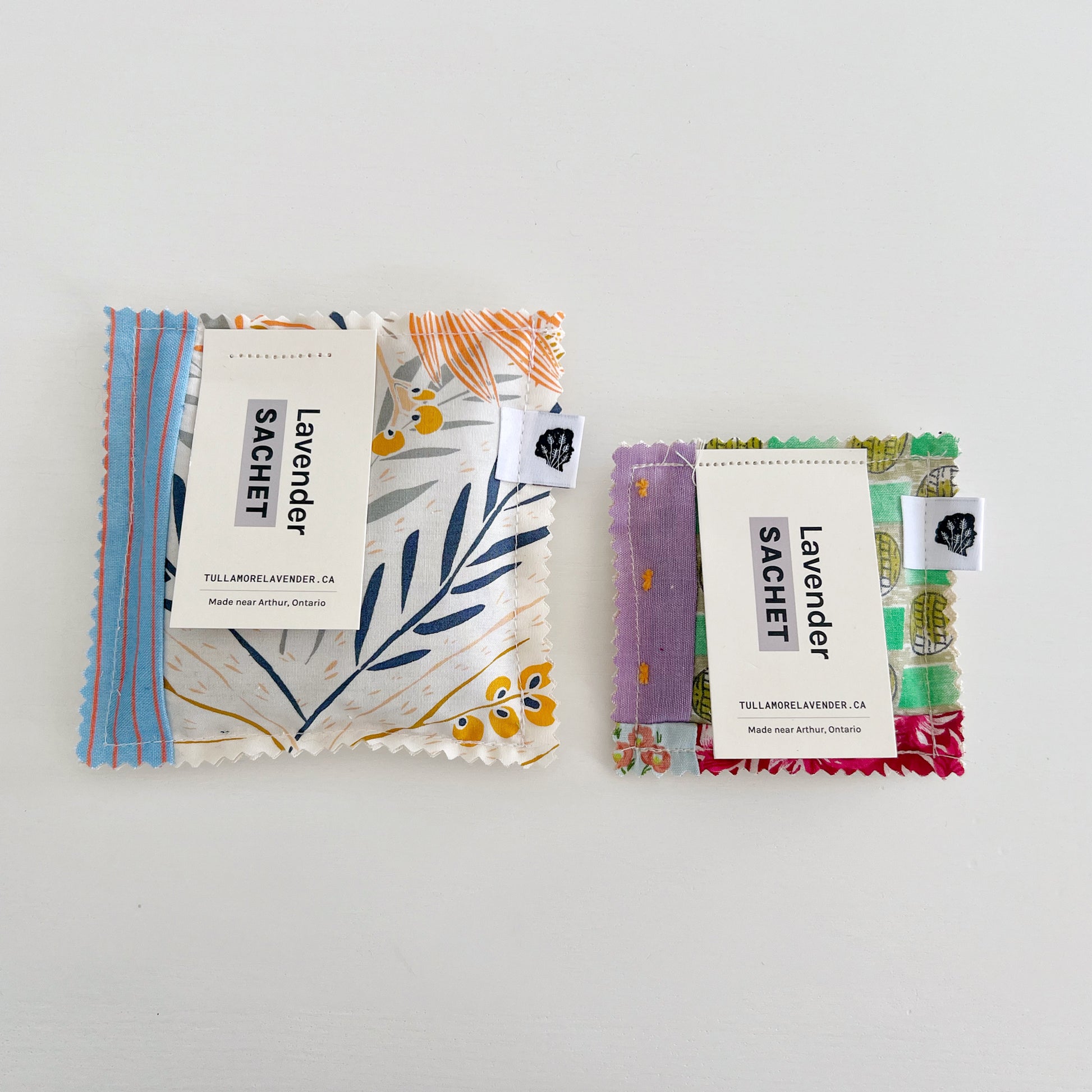 One large and one small fabric sachets lay on white background. Tags say "Lavender Sachet"