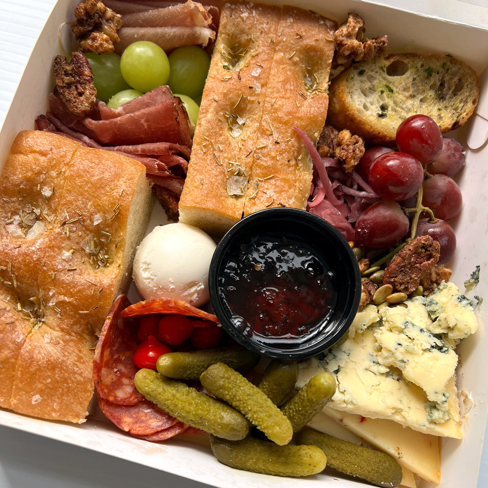 Meat, cheese, bread, pickles, grapes and dip in a rectangle box