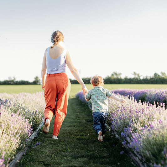 White woman and white child run with backs to camera through blooming lavender field