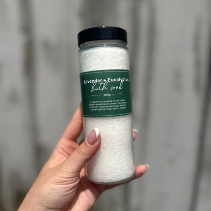 Bottle of lavender and eucalyptus bath salts held by a hand against a neutral background